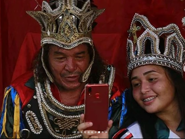 Mestre Antônio e sua filha Fabrisleny com adornos do reisado. Sua filha segura o celular mostrando ao pai.